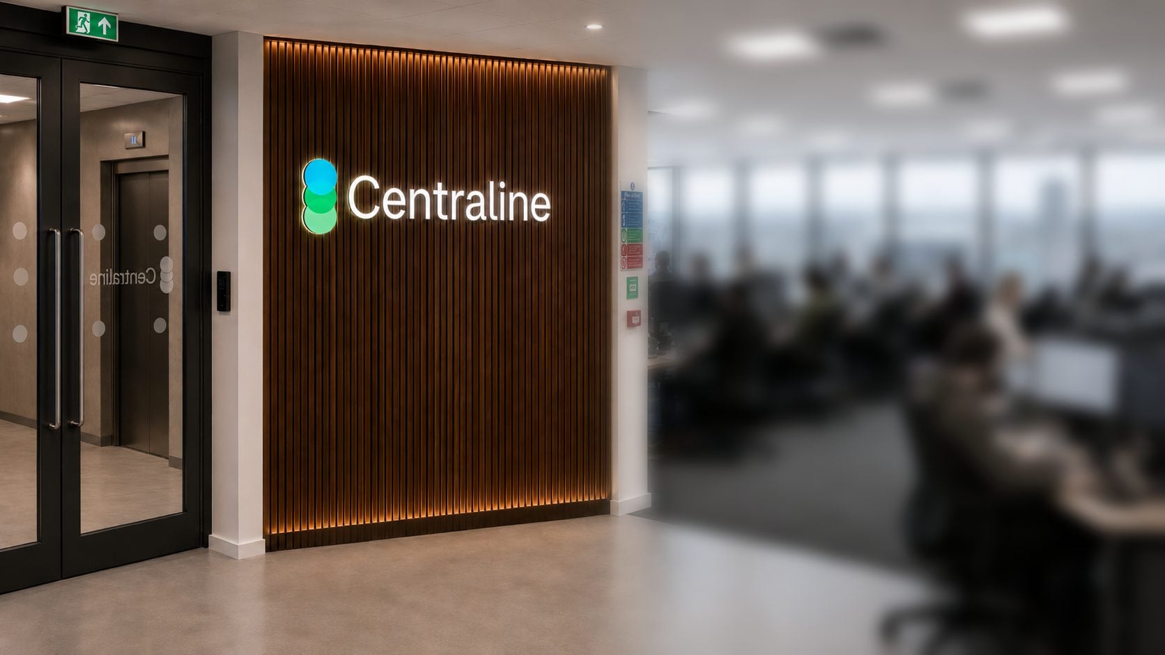 The Centraline office in Cardiff: the lit Centraline sign on a timber wall by the entrance, with the engineering floor working beyond it.